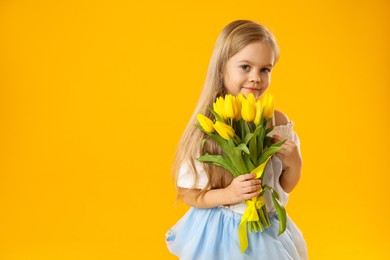 Photo of Cute little girl with beautiful yellow tulips on orange background, space for text. Spring season