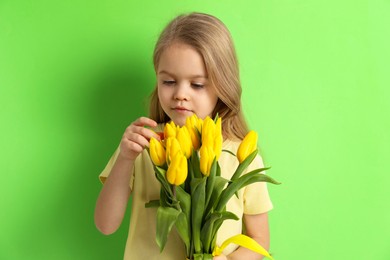 Cute little girl with beautiful yellow tulips on green background. Spring season