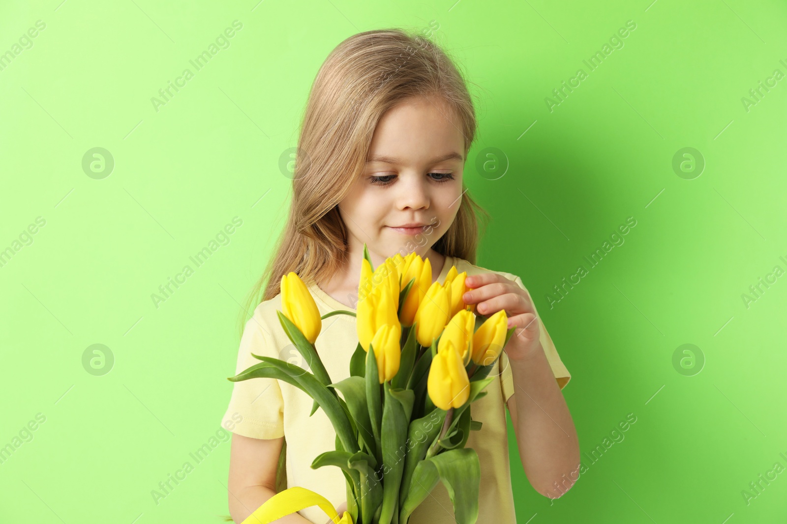 Photo of Cute little girl with beautiful yellow tulips on green background. Spring season