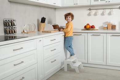 Photo of Little boy with cookies standing on step stool near countertop in kitchen