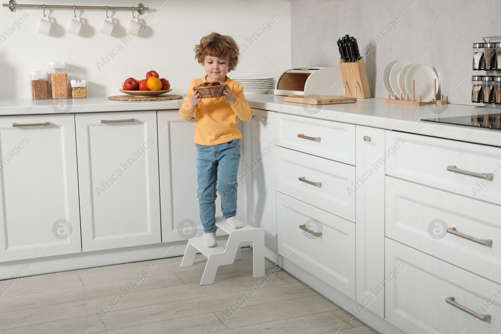 Photo of Little boy with cookies standing on step stool in kitchen