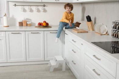 Photo of Little boy sitting on countertop and step stool in kitchen