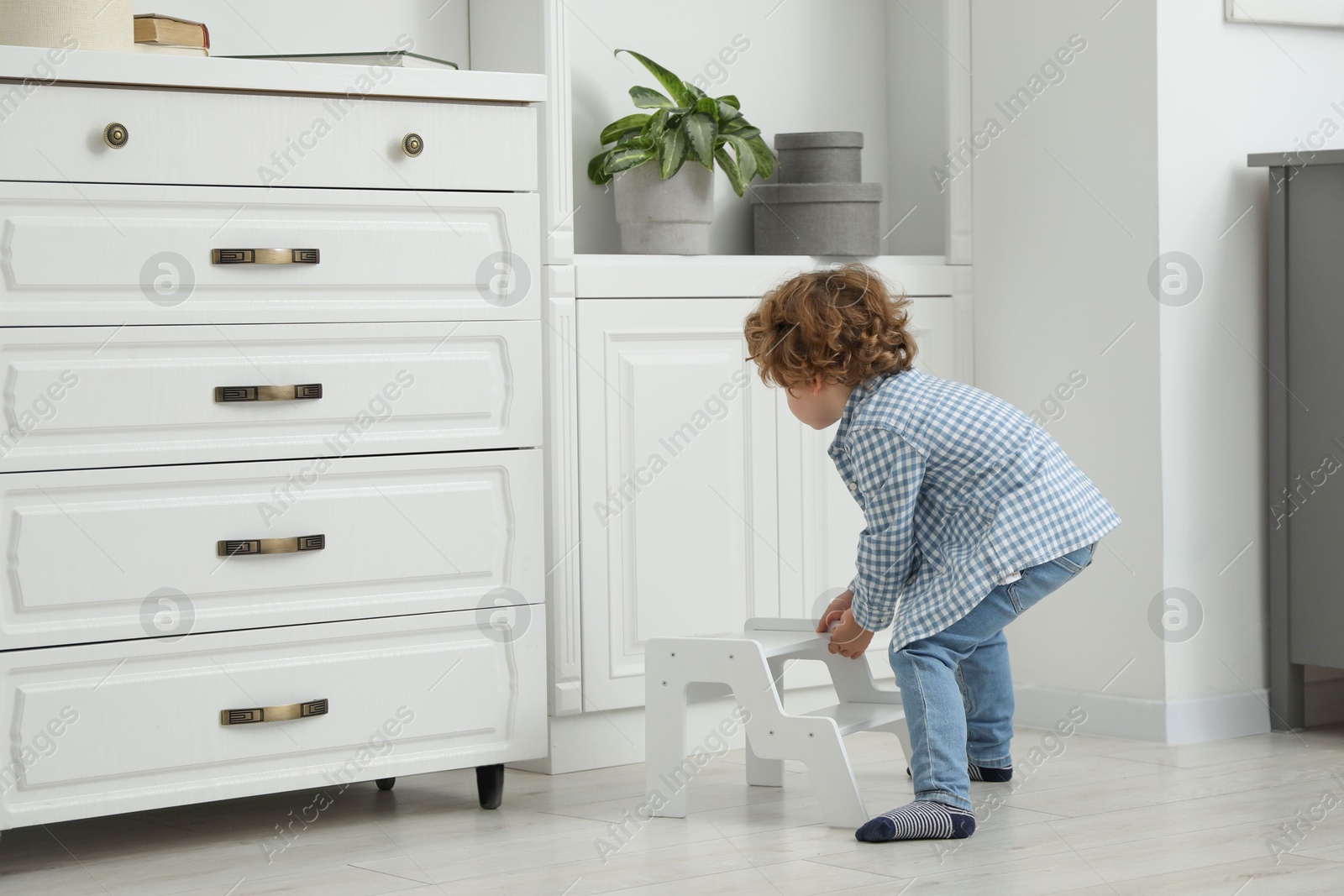 Photo of Little boy with step stool near shelving unit at home