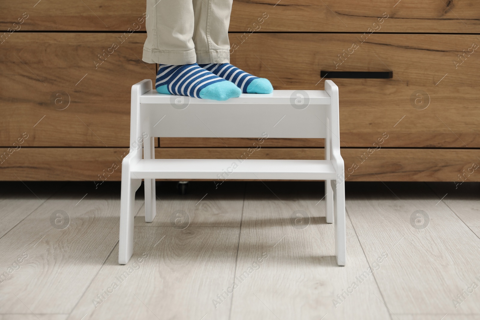 Photo of Little boy with step stool near chest of drawers at home, closeup