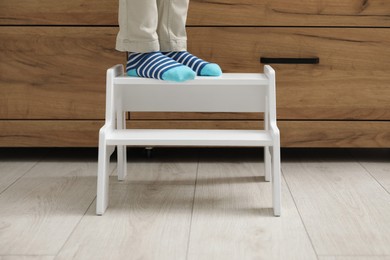 Photo of Little boy with step stool near chest of drawers at home, closeup