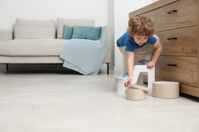 Photo of Little boy reaching for box while standing on step stool near chest of drawers at home