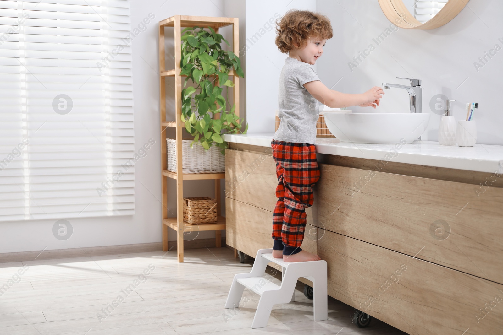 Photo of Little boy standing on step stool near bathroom vanity indoors