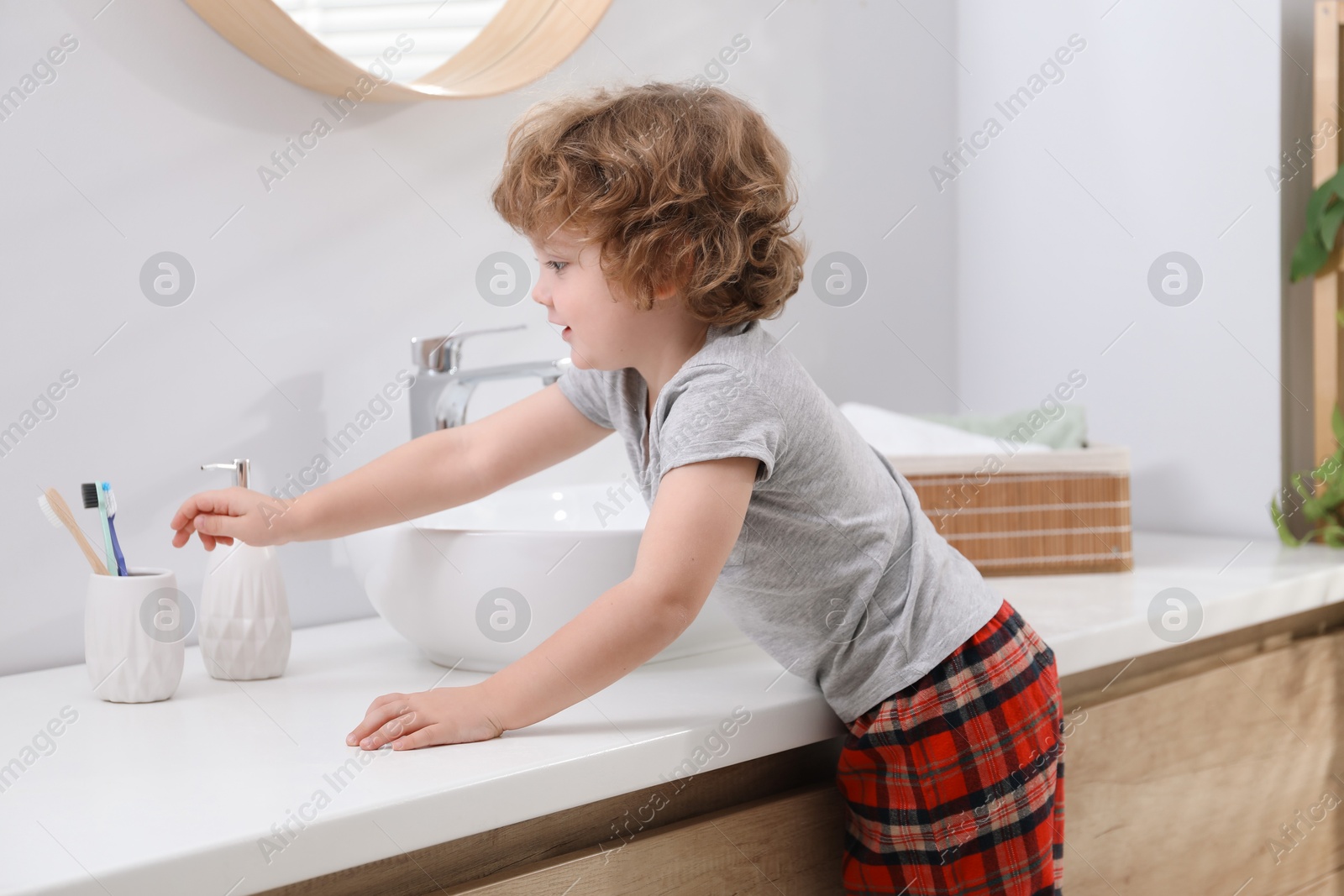 Photo of Little boy taking toothbrush near bathroom vanity indoors