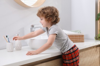 Photo of Little boy taking toothbrush near bathroom vanity indoors