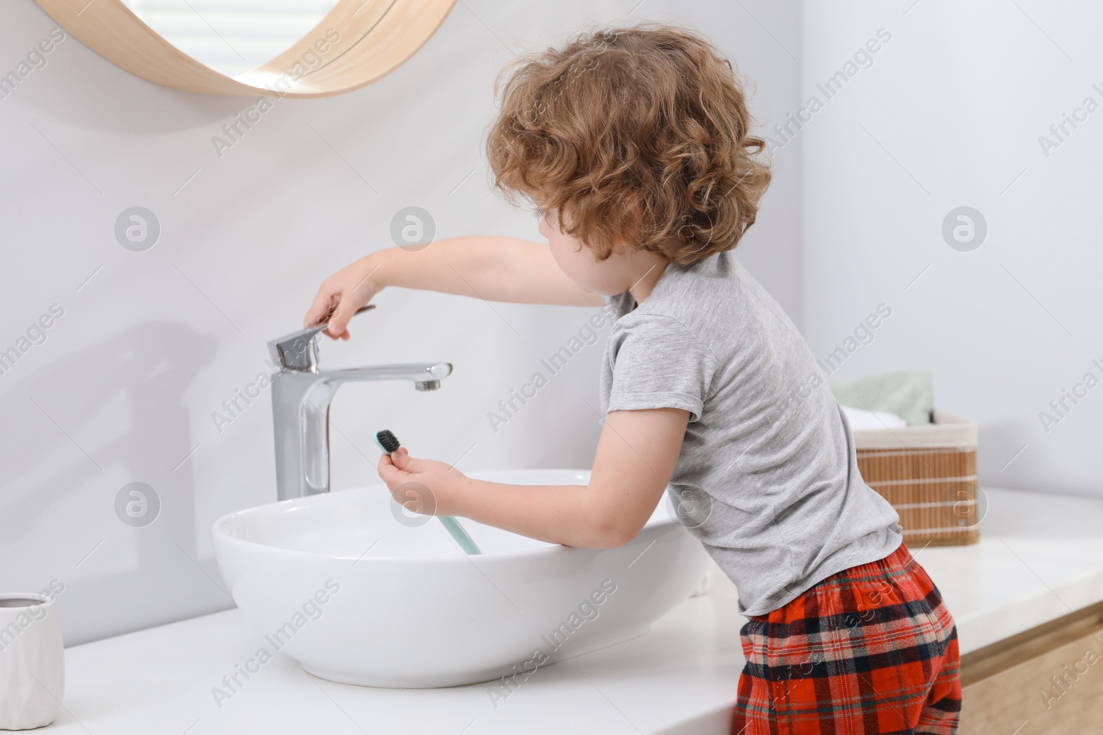 Photo of Little boy with toothbrush near bathroom vanity indoors