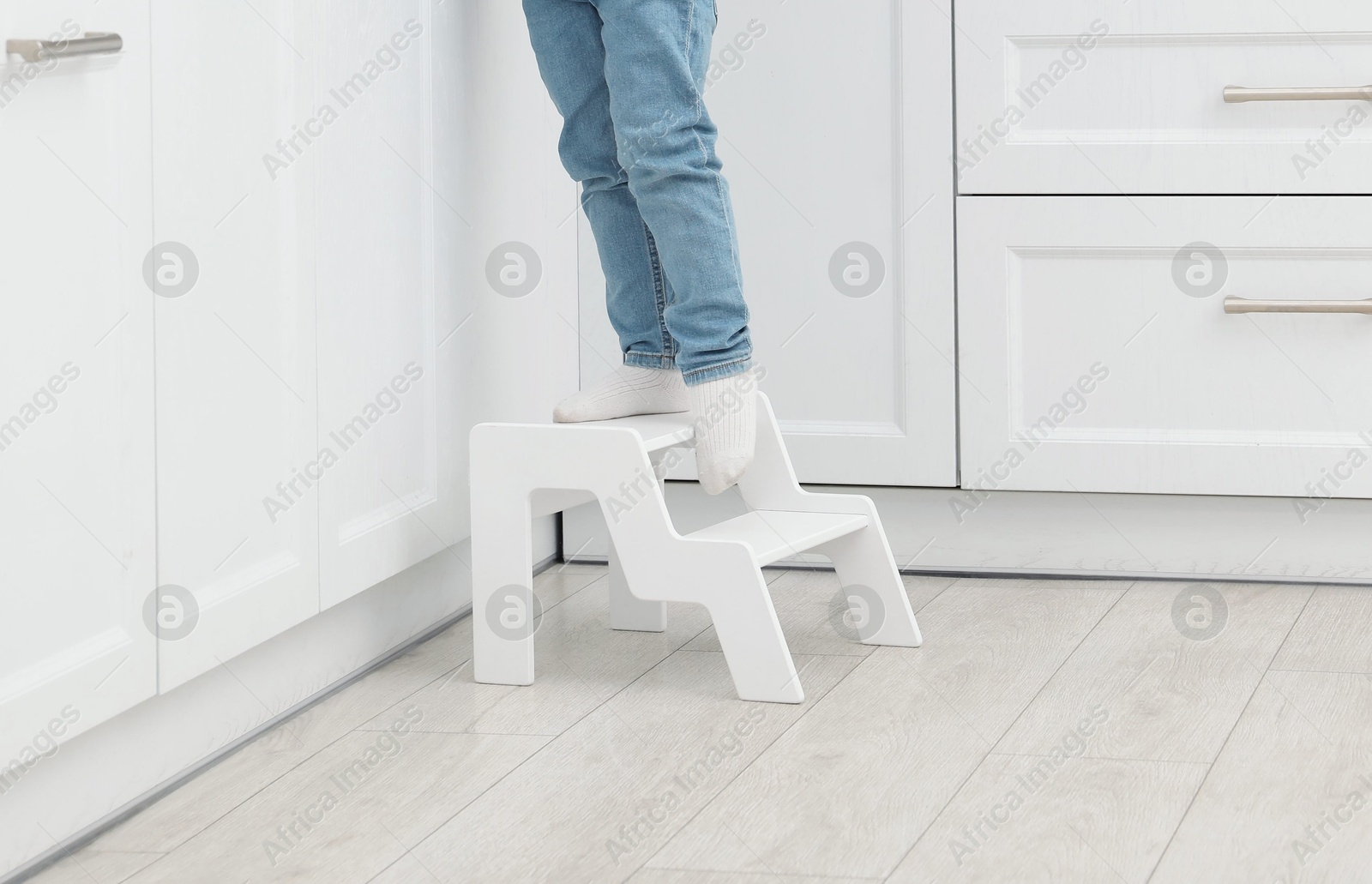 Photo of Little boy with apple standing on step stool in kitchen, closeup