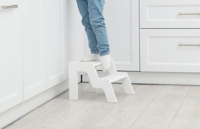 Photo of Little boy with apple standing on step stool in kitchen, closeup