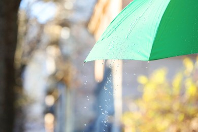 Photo of Open green umbrella under pouring rain outdoors, closeup. Space for text