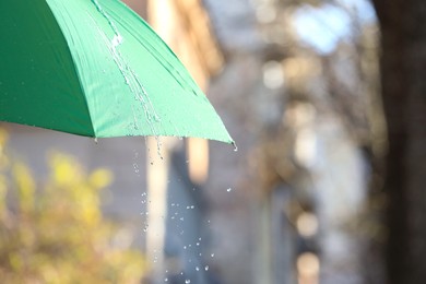 Photo of Open green umbrella under pouring rain outdoors, closeup. Space for text