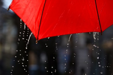 Photo of Open red umbrella under pouring rain outdoors, closeup