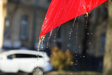 Photo of Open red umbrella under pouring rain outdoors, closeup