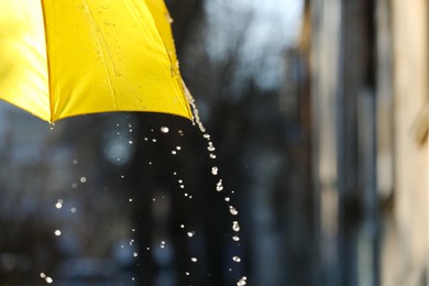 Photo of Open yellow umbrella under pouring rain outdoors, closeup. Space for text