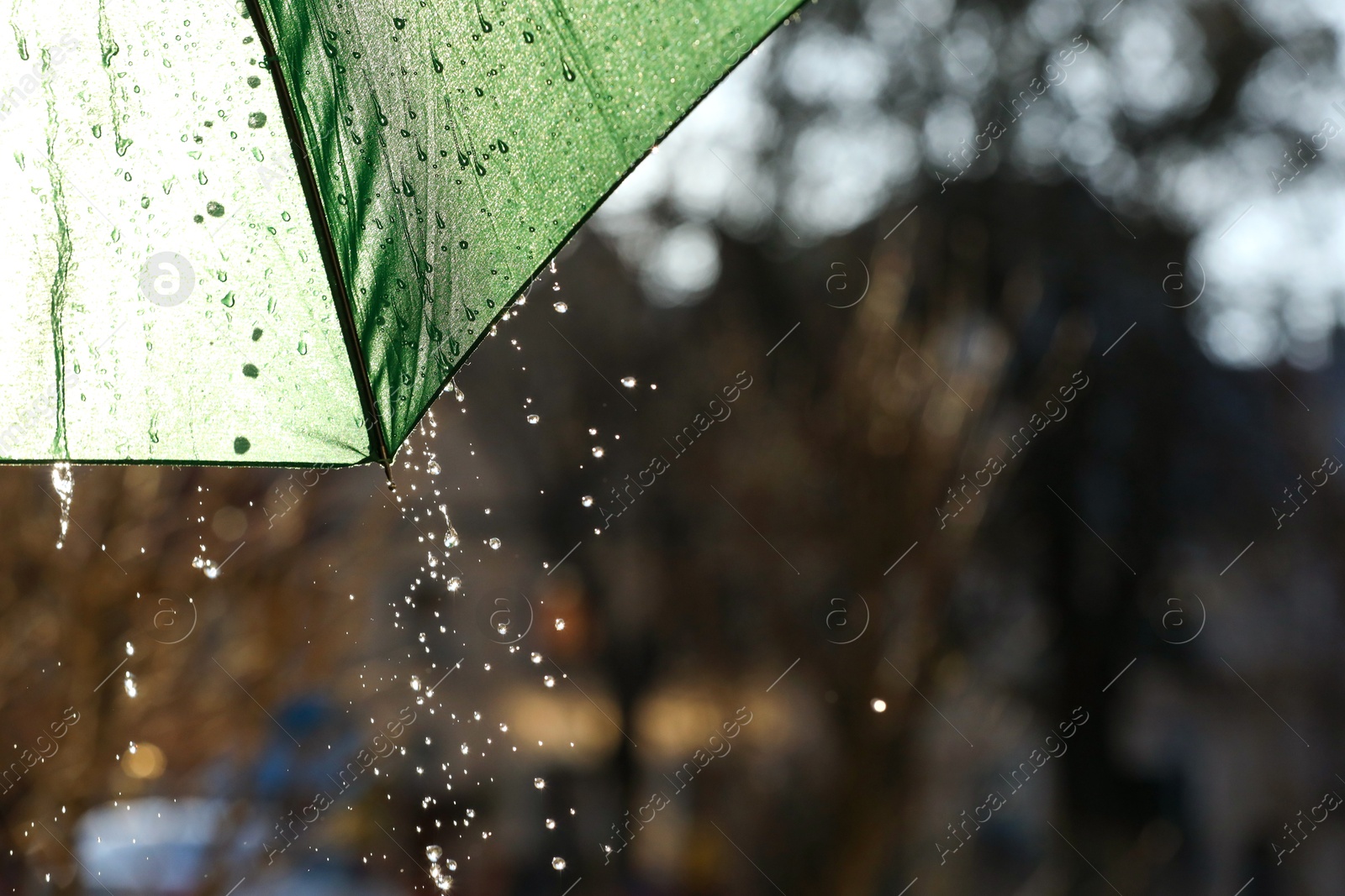 Photo of Open green umbrella under pouring rain outdoors, closeup. Space for text