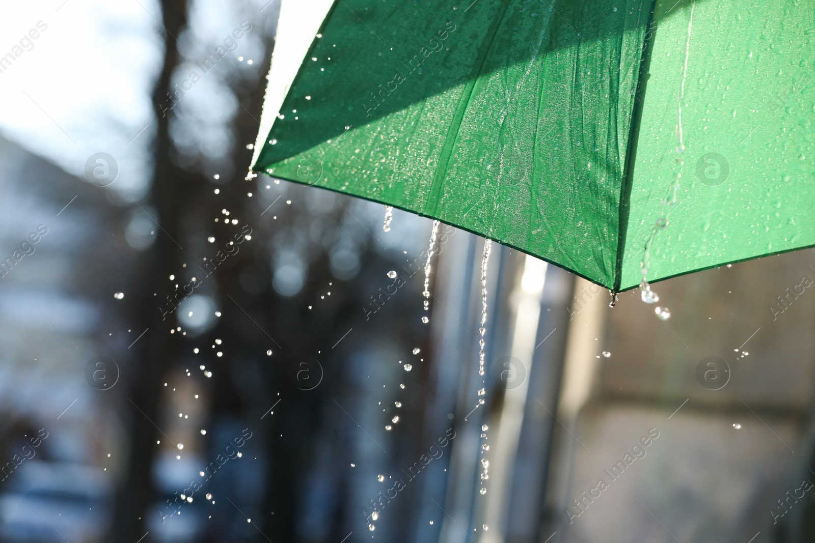 Photo of Open green umbrella under pouring rain outdoors, closeup