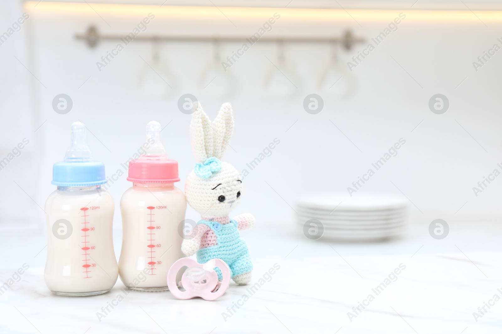 Photo of Feeding bottles with baby formula, pacifier and toy bunny on white table indoors. Space for text