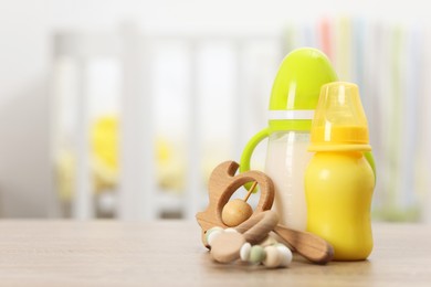 Photo of Feeding bottles with milk and toys on wooden table indoors. Space for text