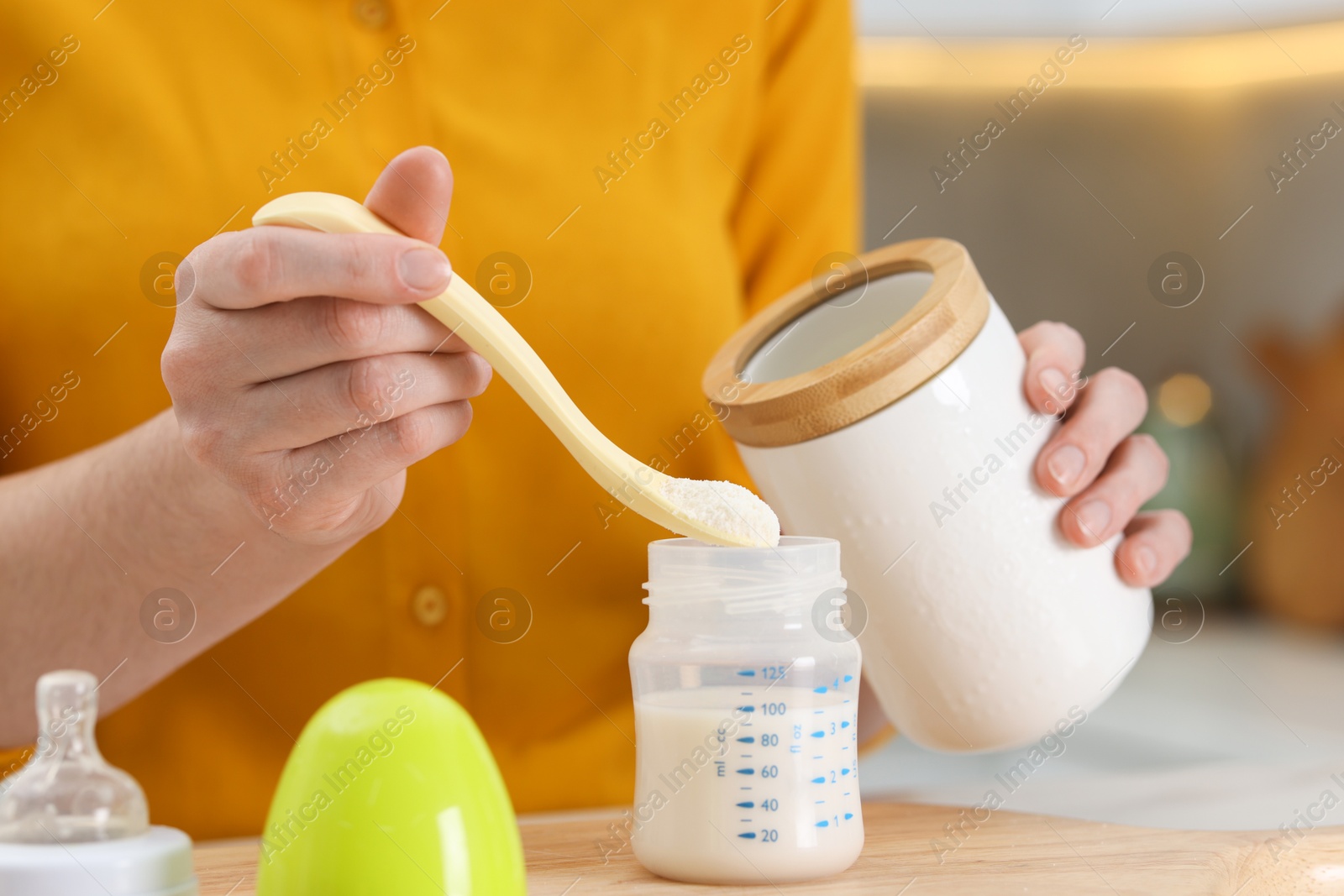 Photo of Mother making baby formula in feeding bottle at table indoors, closeup