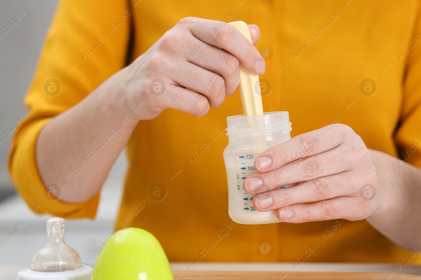 Photo of Mother making baby formula in feeding bottle indoors, closeup