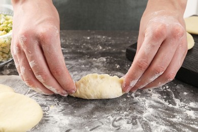 Photo of Woman making pirozhki (stuffed pastry pies) with eggs and dill at gray table indoors, closeup