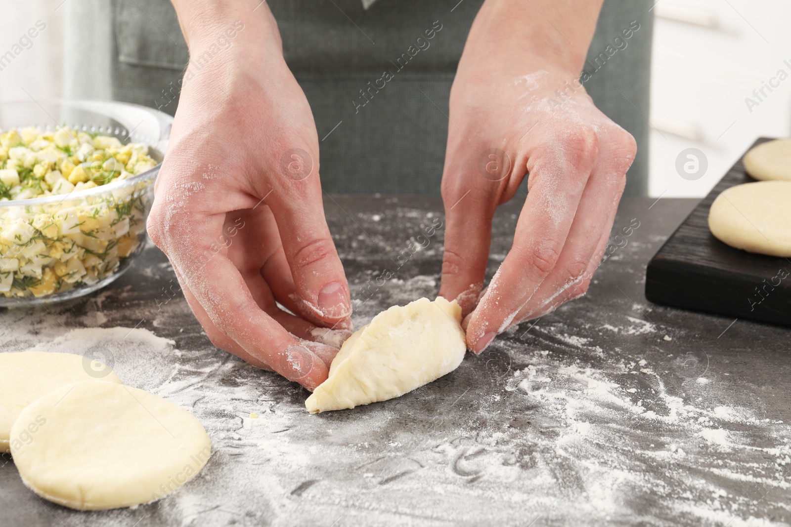 Photo of Woman making pirozhki (stuffed pastry pies) with eggs and dill at gray table indoors, closeup