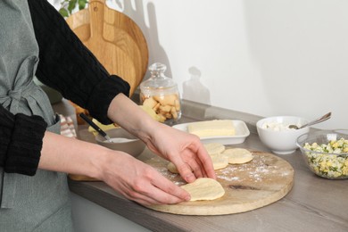 Photo of Woman making pirozhki (stuffed pastry pies) at countertop indoors, closeup