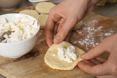 Photo of Woman making pirozhki (stuffed pastry pies) with cottage cheese at table, closeup