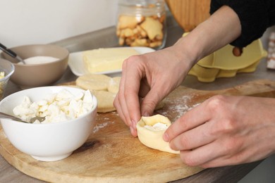 Photo of Woman making pirozhki (stuffed pastry pies) with cottage cheese at table, closeup