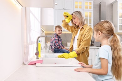 Tired housewife washing dishes while her kids playing in kitchen