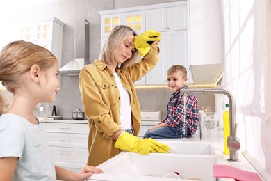 Tired housewife washing dishes while her kids playing in kitchen