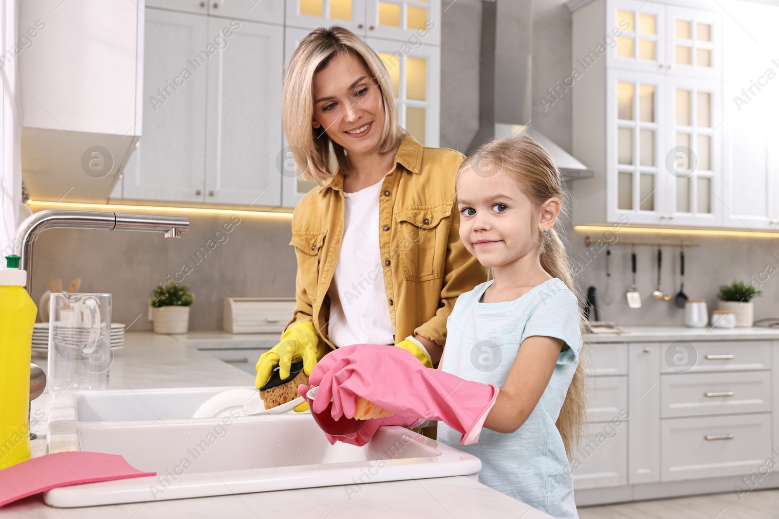 Photo of Happy housewife and her daughter washing dishes in kitchen together