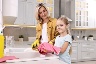 Happy housewife and her daughter washing dishes in kitchen together