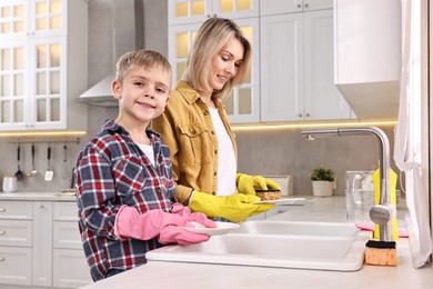 Happy housewife and her son washing dishes in kitchen together