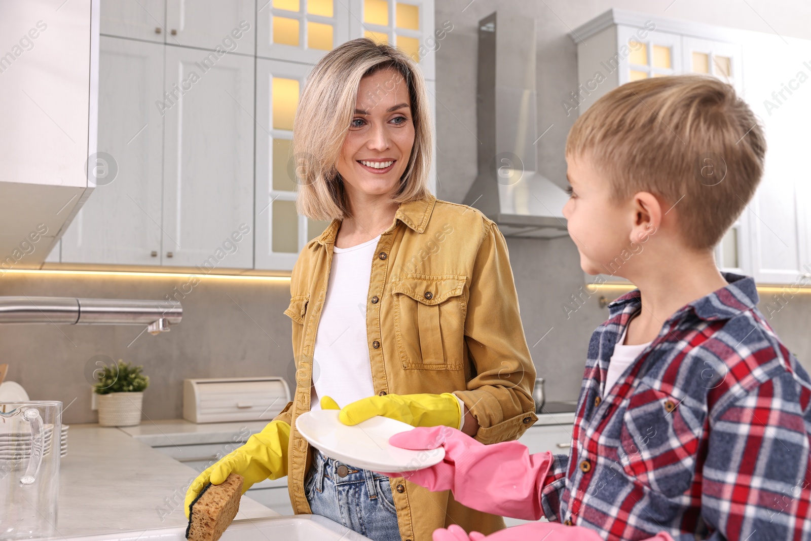 Photo of Happy housewife and her son washing dishes in kitchen together