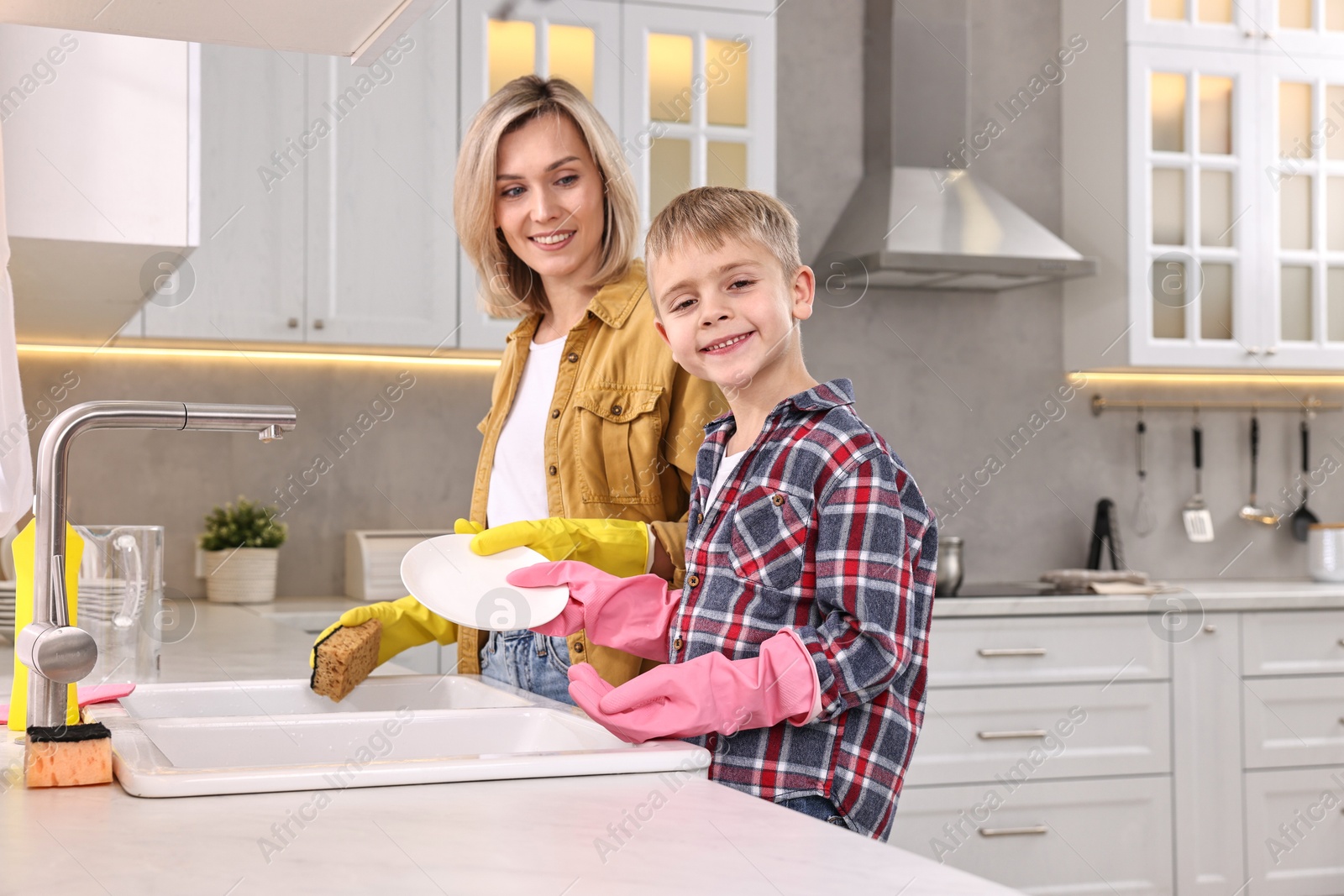 Photo of Happy housewife and her son washing dishes in kitchen together