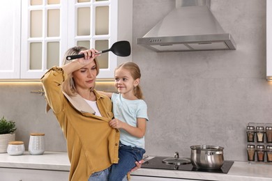 Photo of Tired housewife holding her daughter while cooking in kitchen