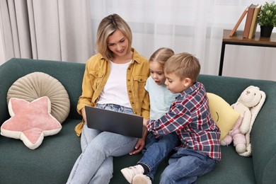 Housewife spending time with her kids and using laptop on couch at home