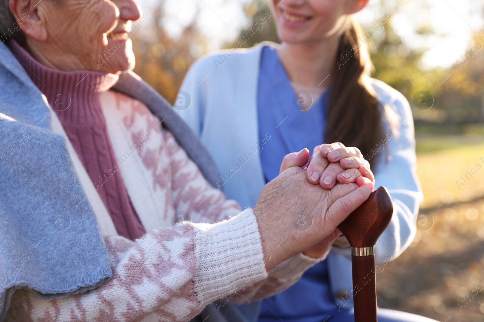 Photo of Elderly woman with walking cane and her caregiver in park, closeup