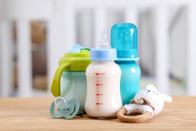 Photo of Feeding bottles with milk, toy and pacifier on wooden table indoors