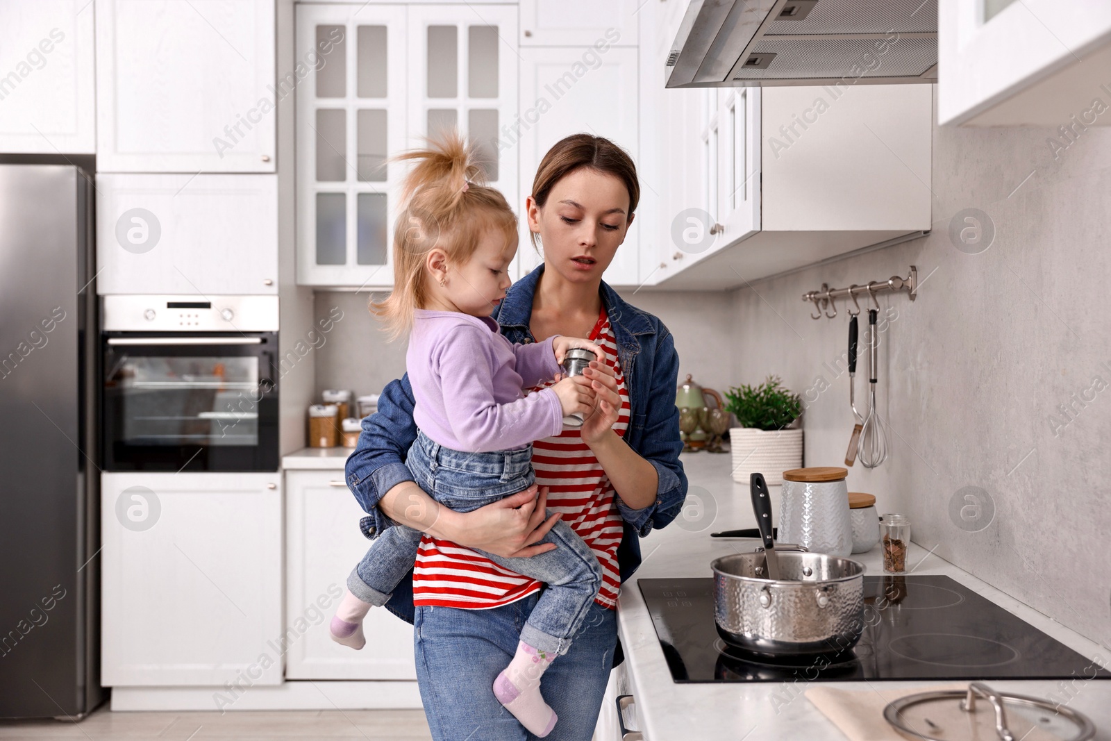 Photo of Busy housewife cooking with her little daughter in kitchen