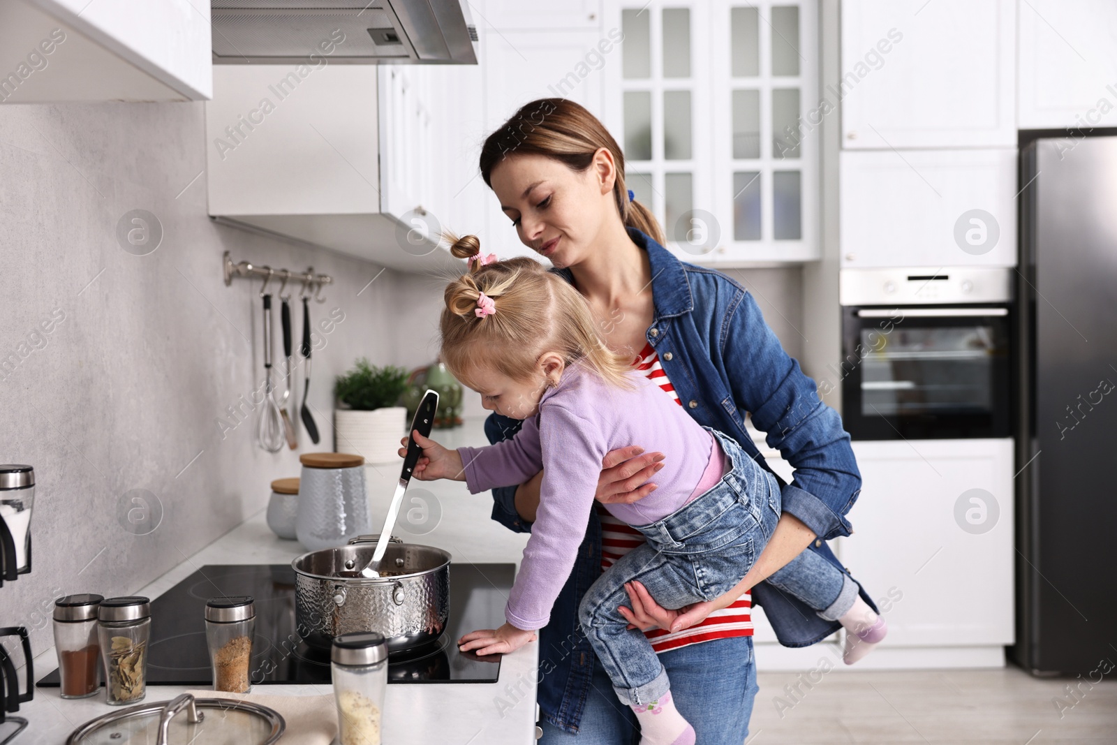 Photo of Busy housewife cooking with her little daughter in kitchen