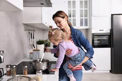 Busy housewife cooking with her little daughter in kitchen