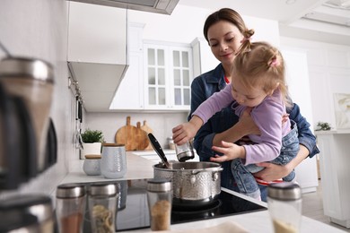 Photo of Housewife cooking with her little daughter in kitchen, low angle view