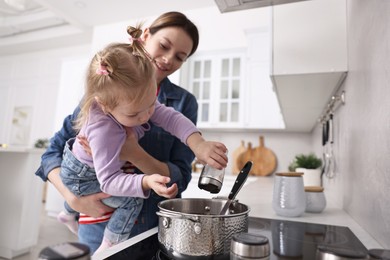 Smiling housewife cooking with her little daughter in kitchen