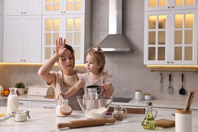 Tired housewife cooking with her little daughter at marble table in kitchen