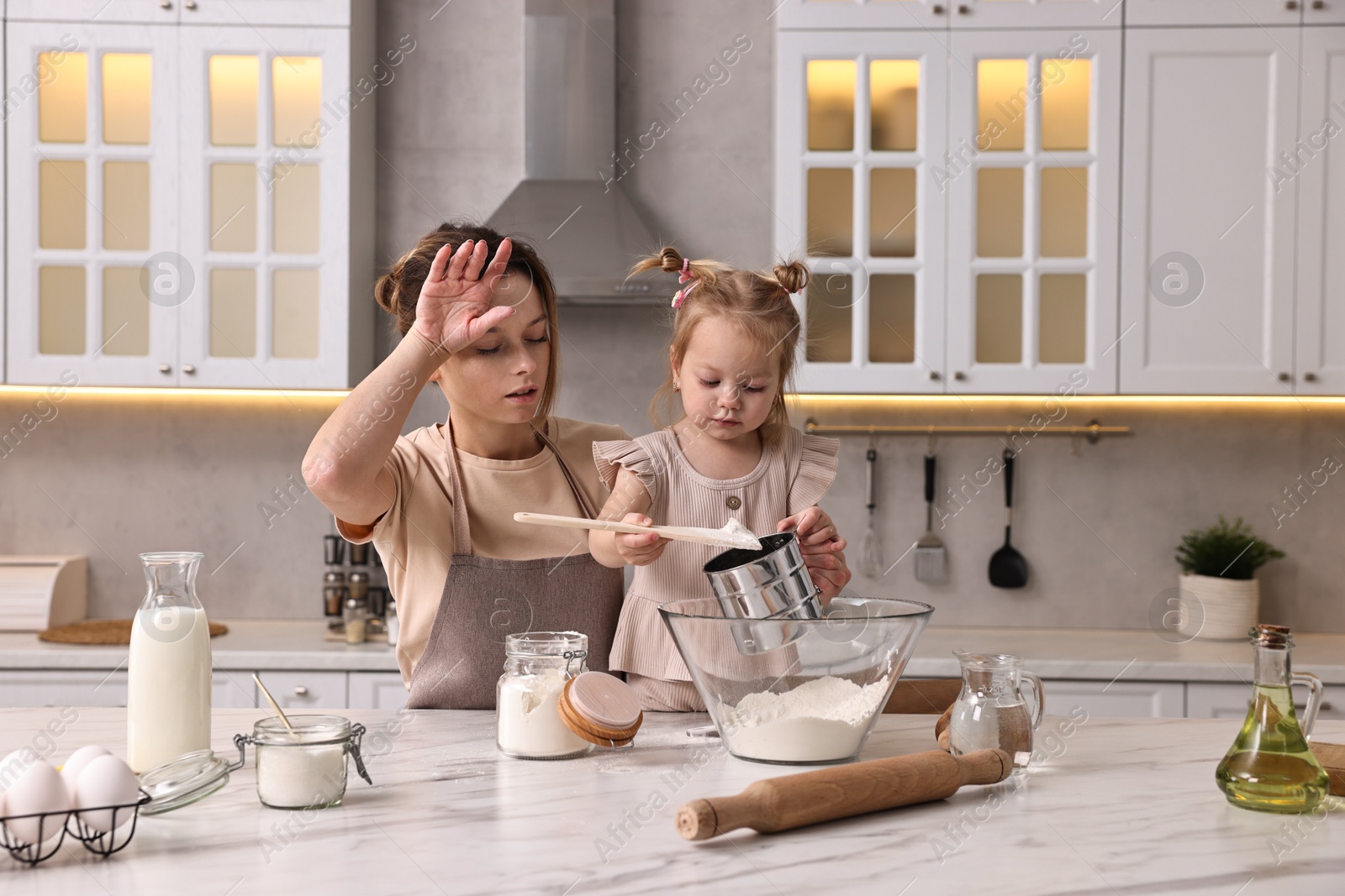 Photo of Tired housewife cooking with her little daughter at marble table in kitchen